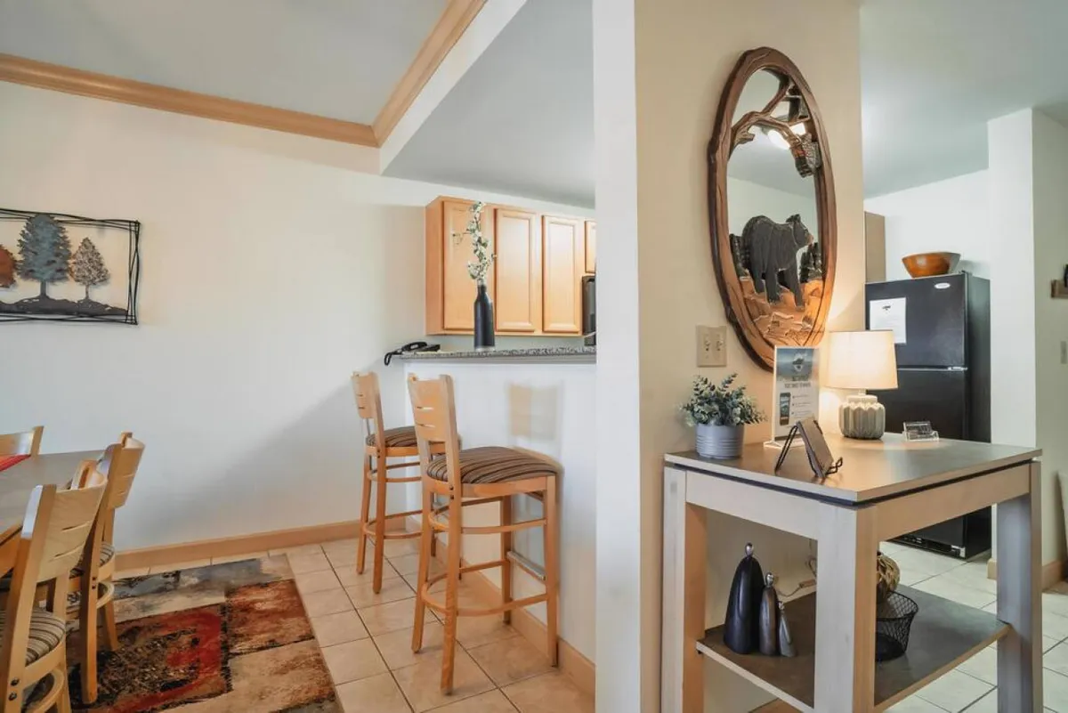 This photo captures a combined kitchen and dining area, featuring a dining table, bar stools, a decorative mirror, and the kitchen visible in the background. The setup is ideal for both family meals and friendly gatherings, providing context for how the spaces flow together.