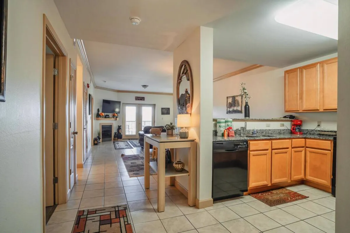 A spacious open-plan area combining the kitchen, dining table, and living room. Large windows offer glimpses of outdoor views, and a fireplace adds an extra layer of coziness. The space is designed for both relaxing and socializing, with ample seating and natural light.