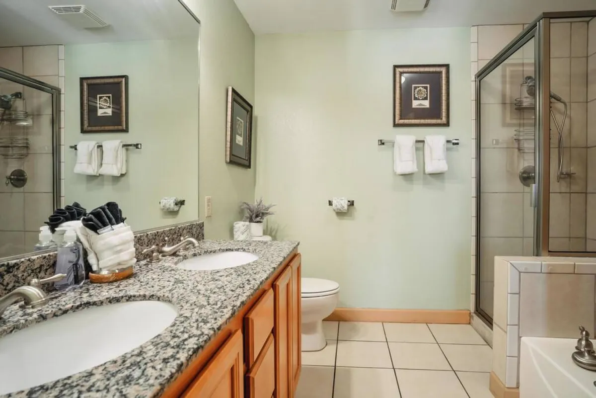A luxurious bathroom featuring a double sink with a granite countertop, a glass-enclosed shower, and a separate bathtub. Elegant framed artwork and soft lighting create a spa-like, tranquil setting ideal for unwinding.